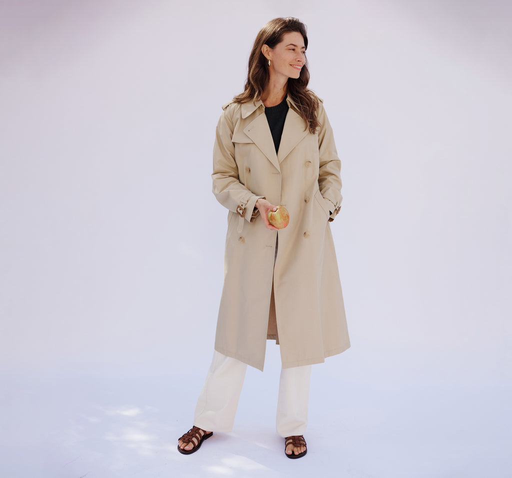 woman wearing nili lotan trench coat with white jeans holding an apple